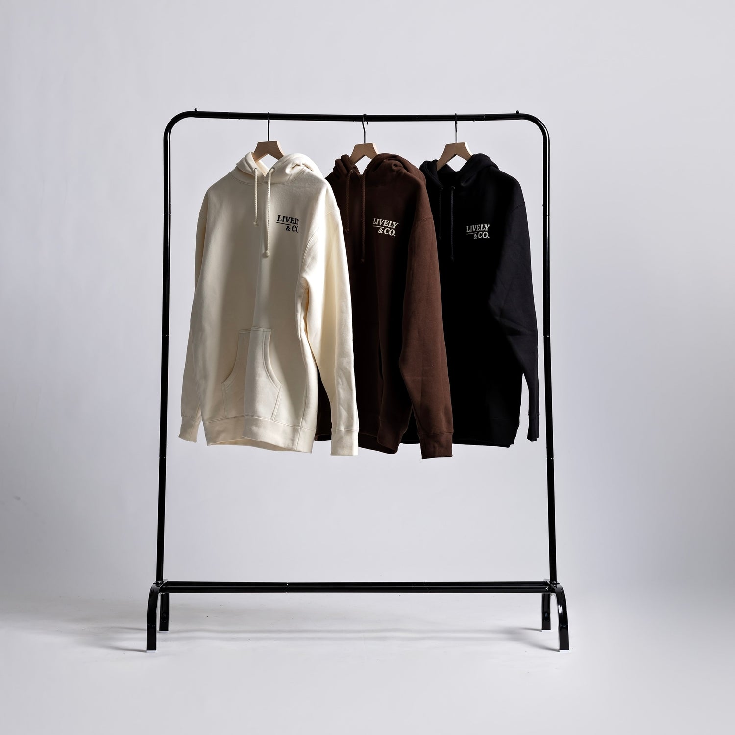Black clothing rack with three hoodies on a white background